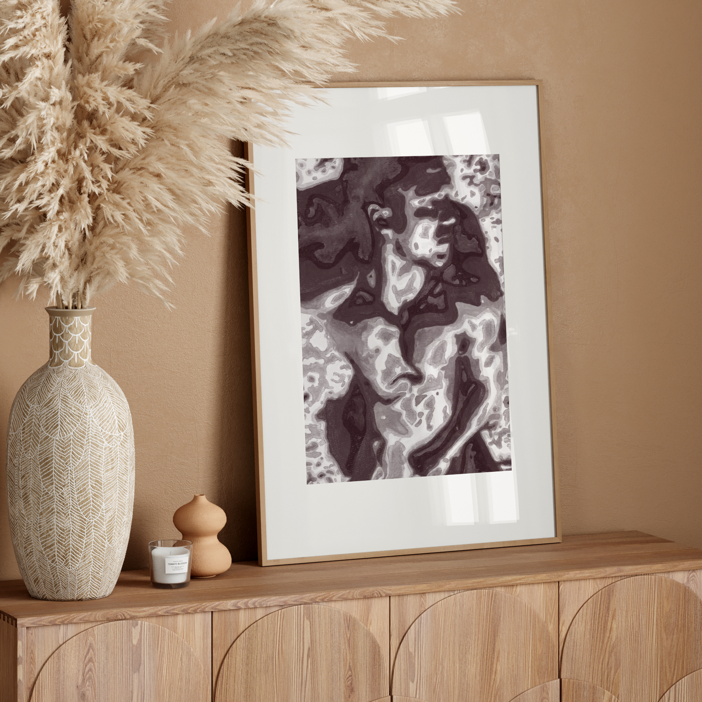Decorative setup with a vase, candle, and framed artwork on a wooden console against a beige wall.