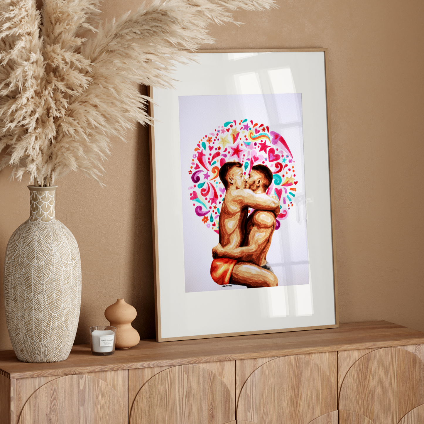 Framed artwork of two people embracing with a colorful design on a wooden sideboard against a beige wall.