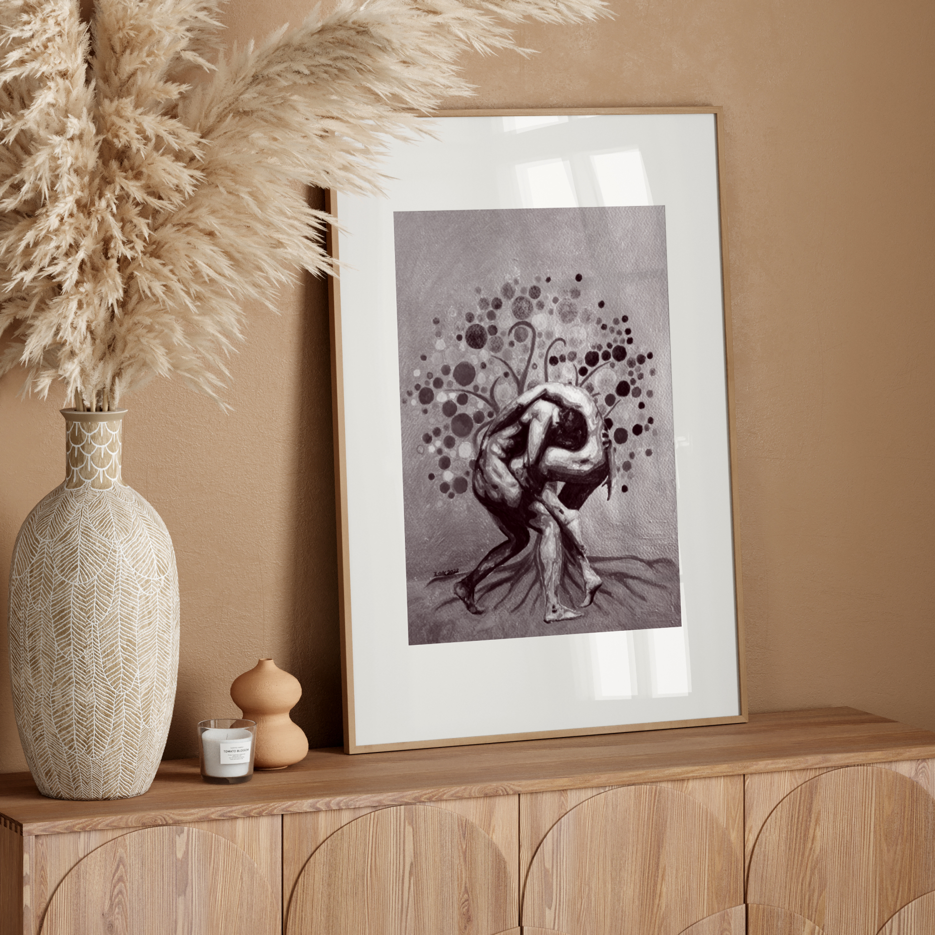 Decorative setup with a vase, candle, and framed artwork on a wooden console against a beige wall.