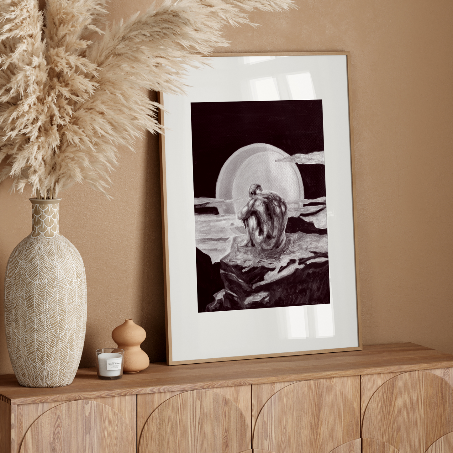 Decorative setup with a vase, candle, and framed artwork on a wooden console against a beige wall.