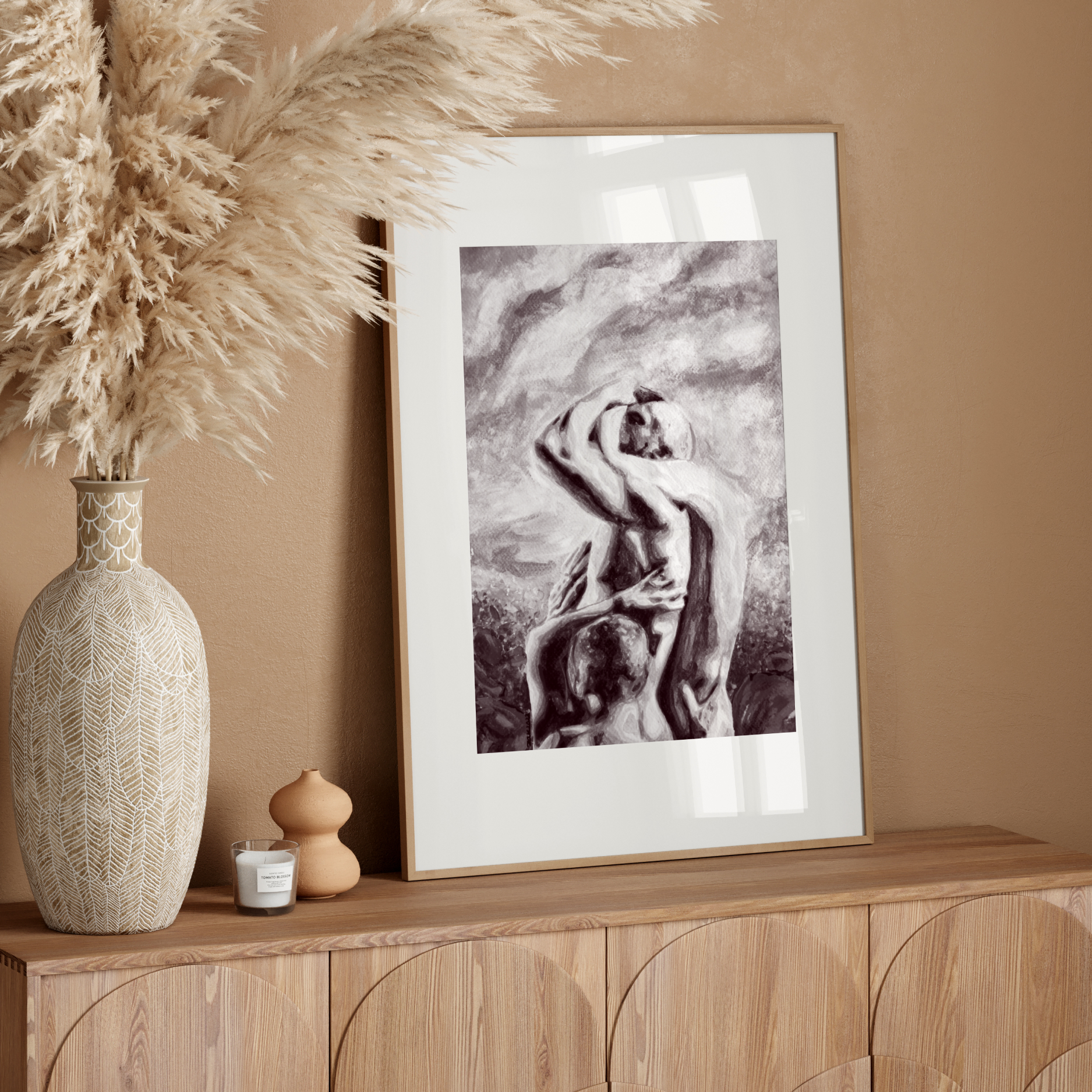 Decorative setup with a vase, candle, and framed artwork on a wooden console against a beige wall.
