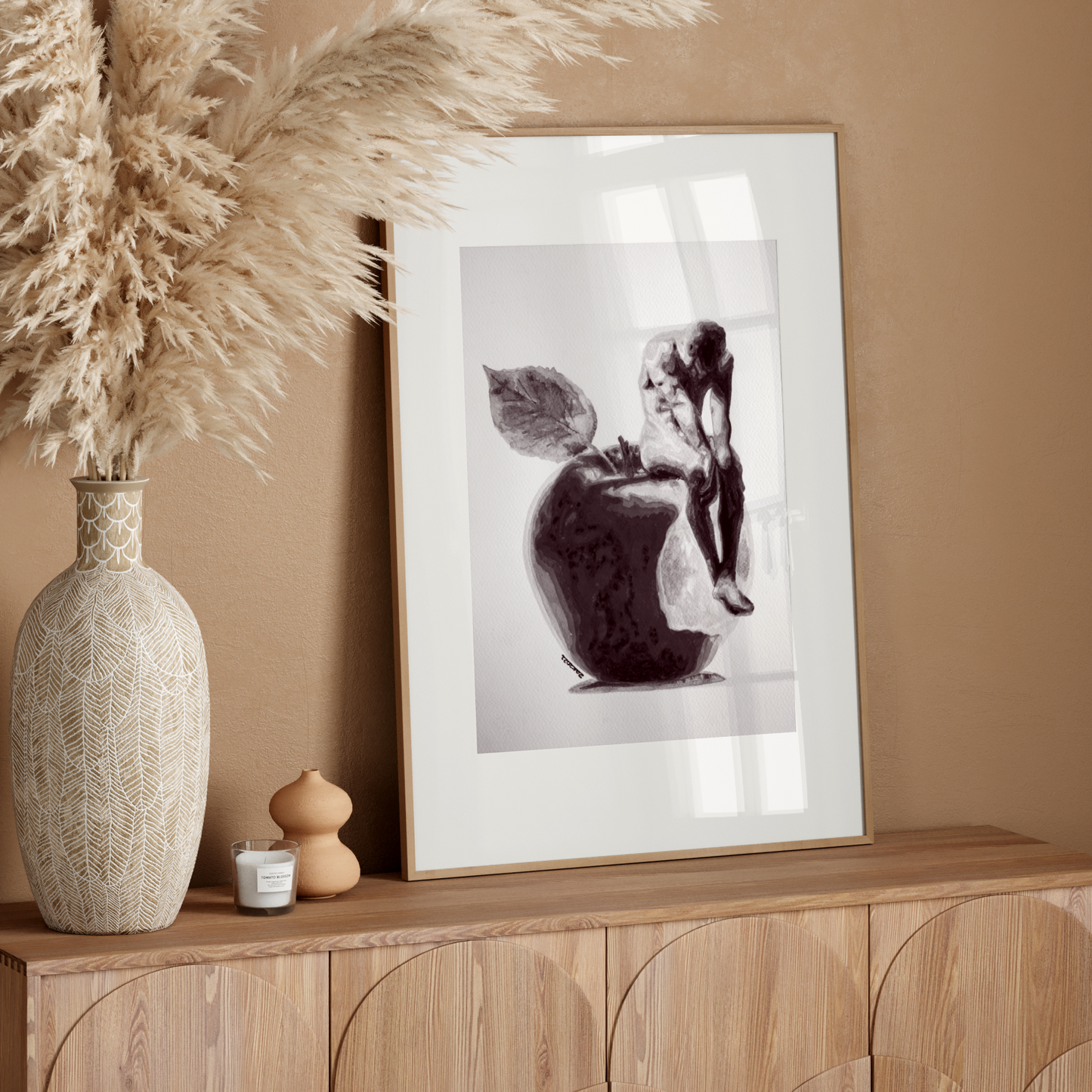 Decorative setup with a vase, candle, and framed artwork on a wooden console against a beige wall.