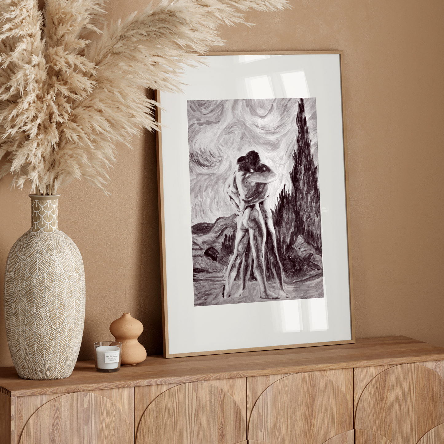 Framed artwork on a wooden console table with decorative vase and pampas grass against a beige wall.