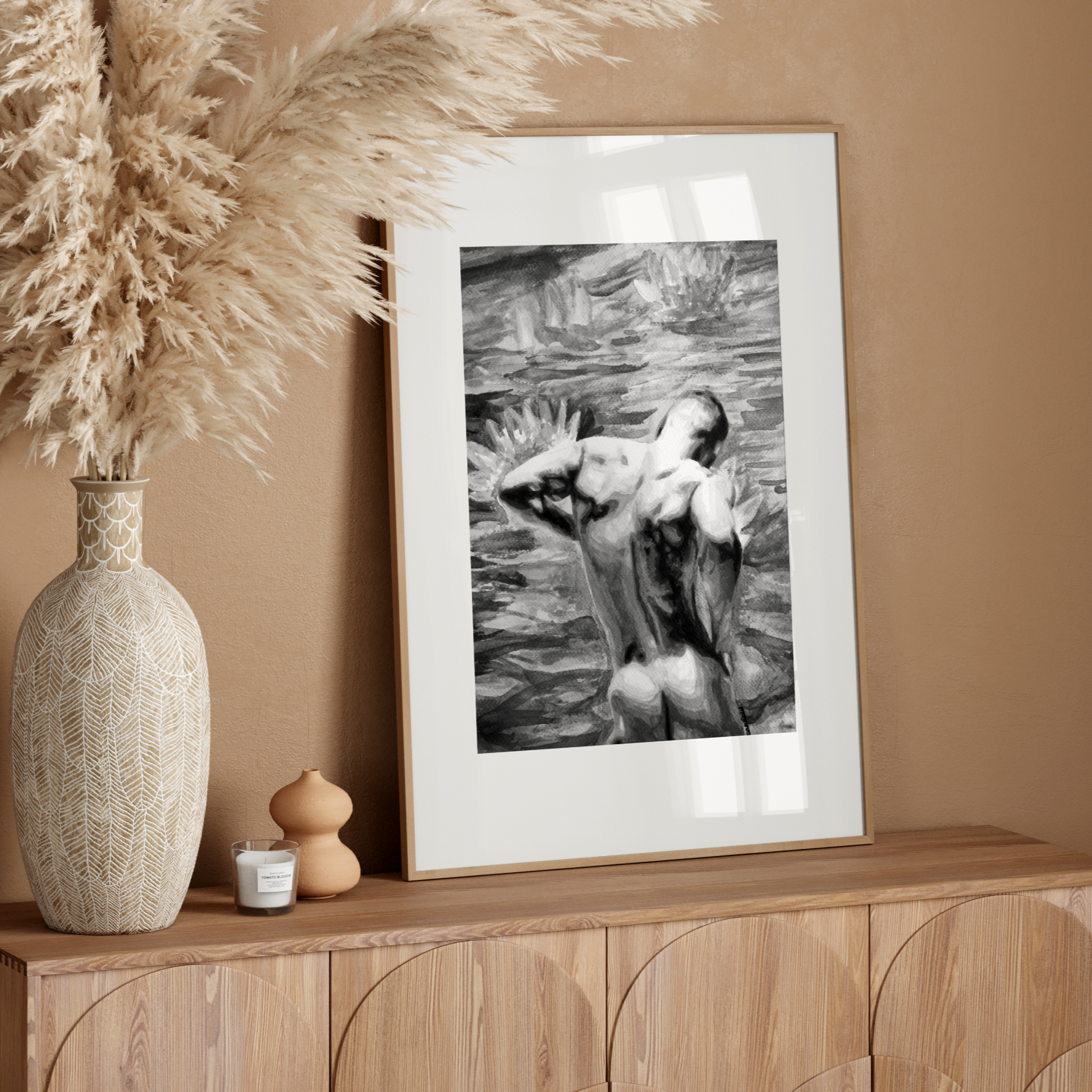 Framed black and white artwork on a wooden sideboard with decorative vase and pampas grass.