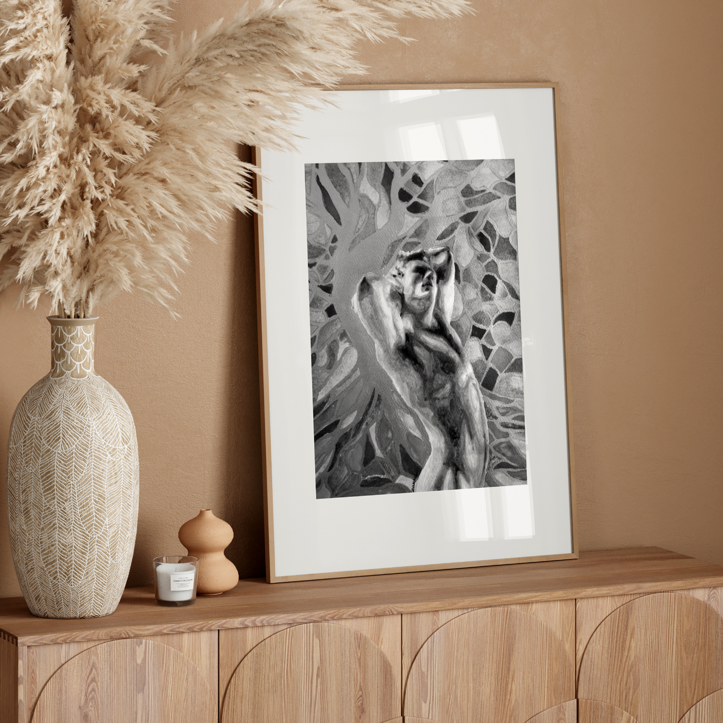 Decorative setup with a vase, candle, and framed artwork on a wooden console against a beige wall.