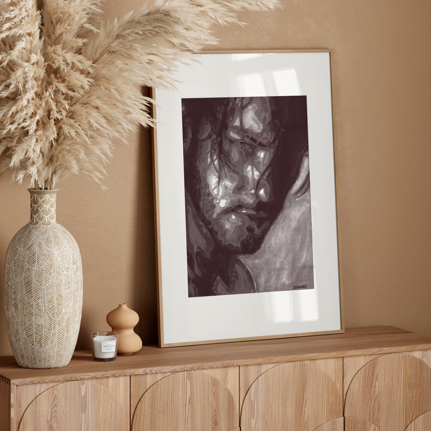 Decorative setup with a vase, candle, and framed artwork on a wooden console against a beige wall.