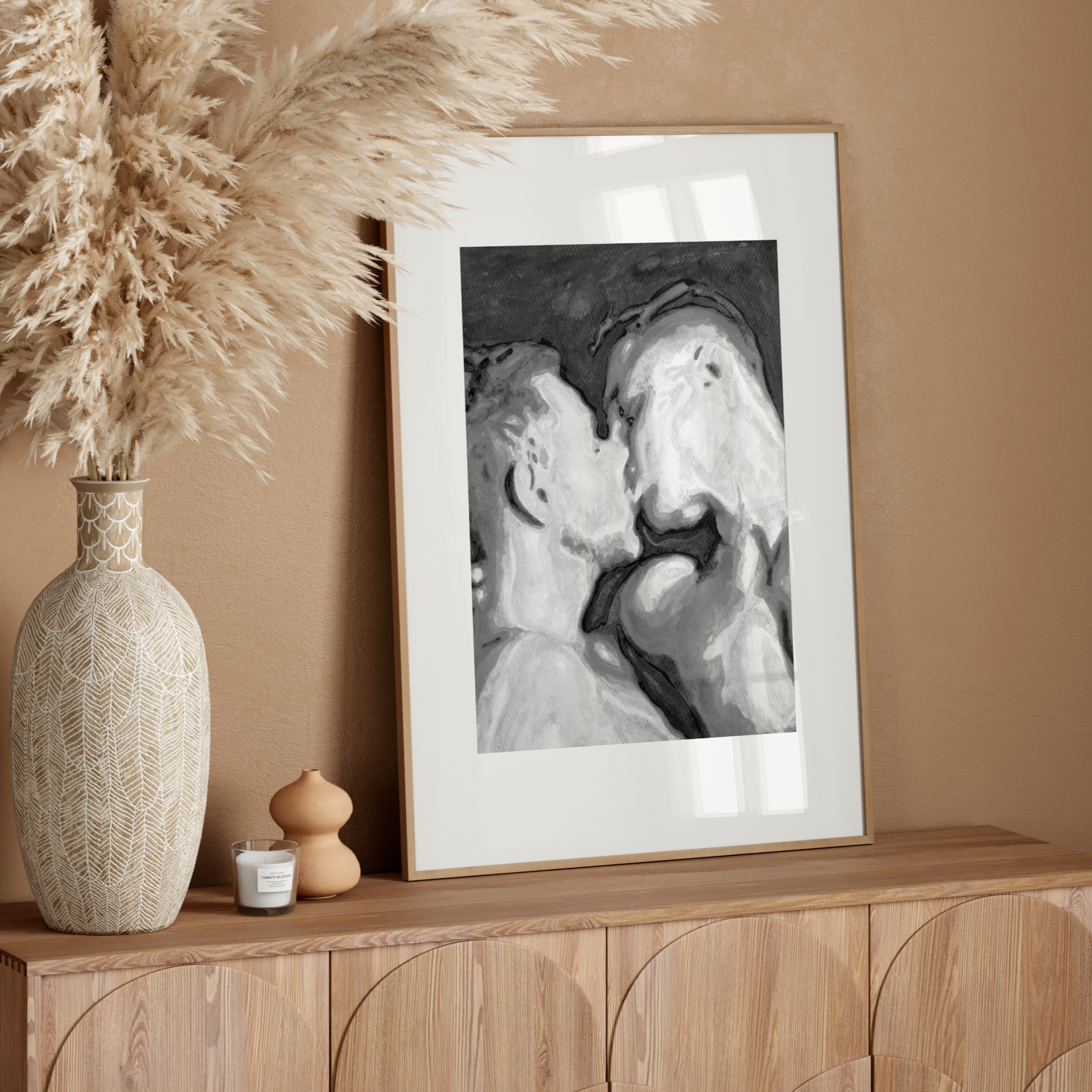 Decorative setup with a vase, candle, and framed artwork on a wooden console against a beige wall.