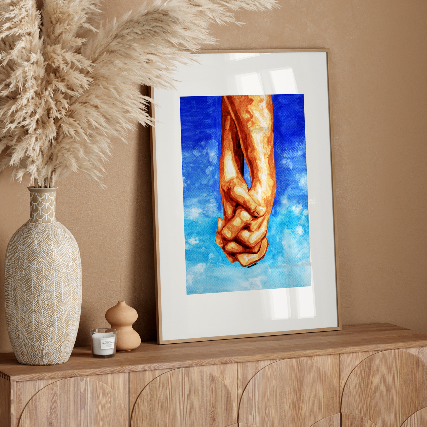 Framed artwork of hands holding a heart on a wooden sideboard with decorative elements.