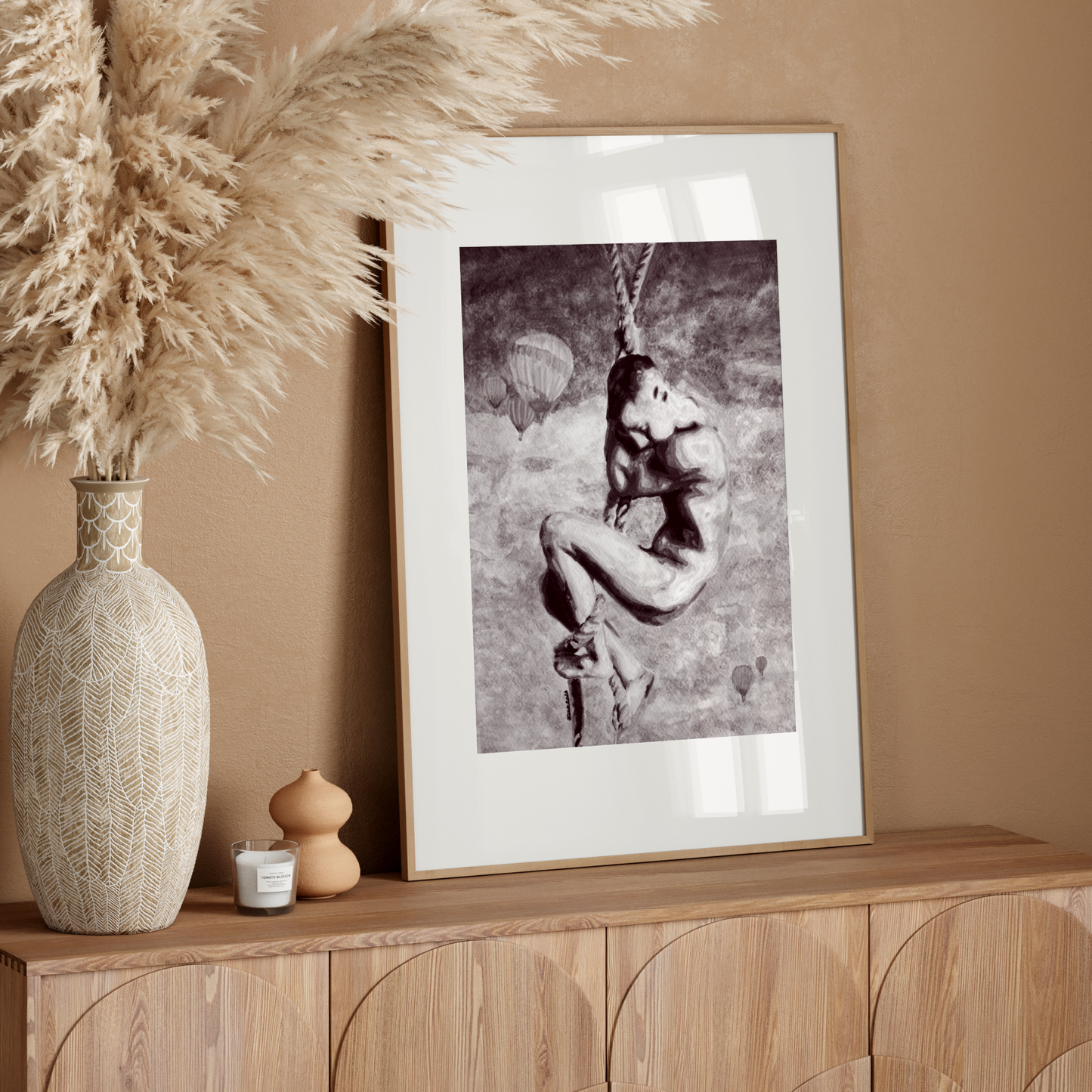 Decorative setup with a vase, candle, and framed black and white print on a wooden console against a beige wall.