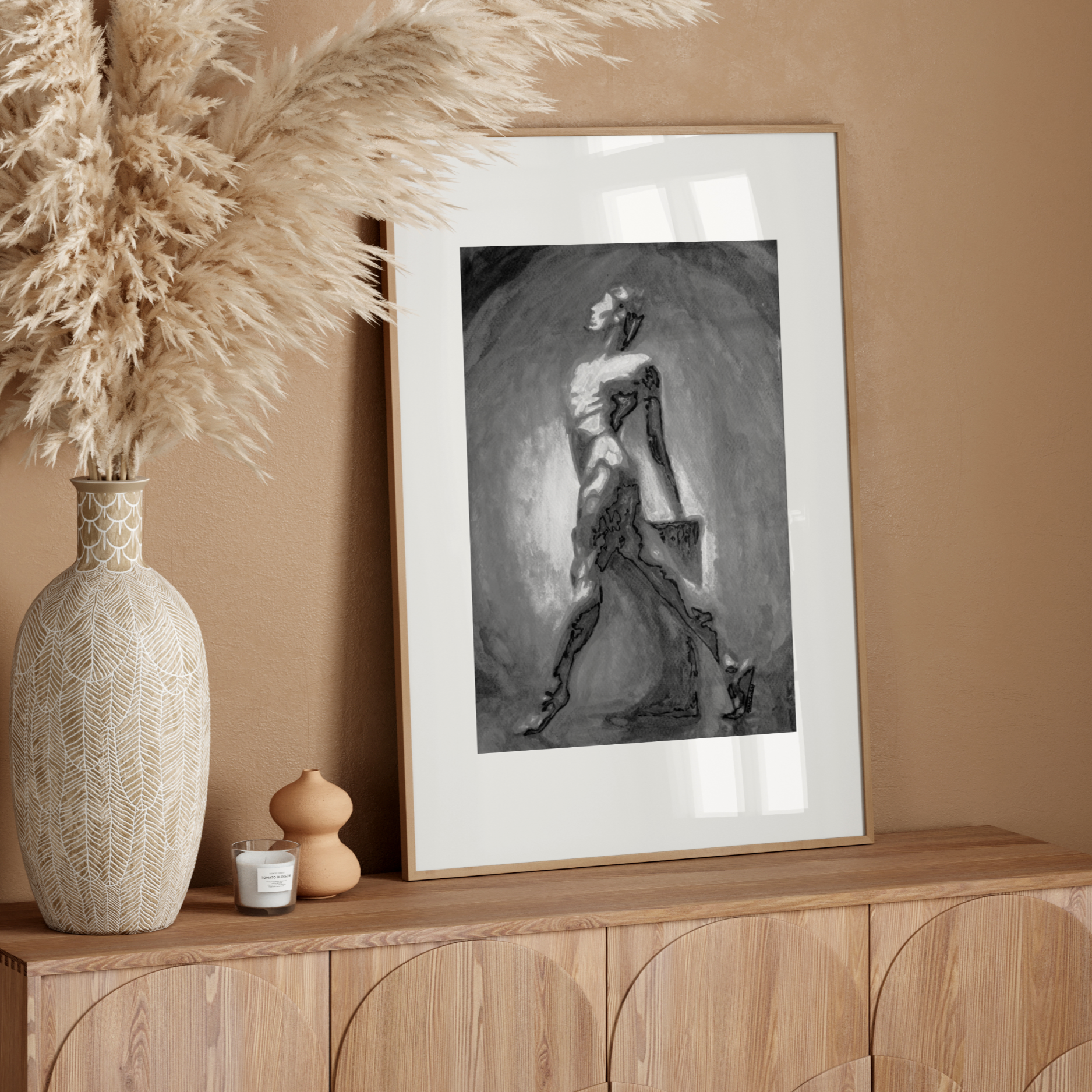 Framed black and white artwork on a wooden sideboard with decorative vase and pampas grass.