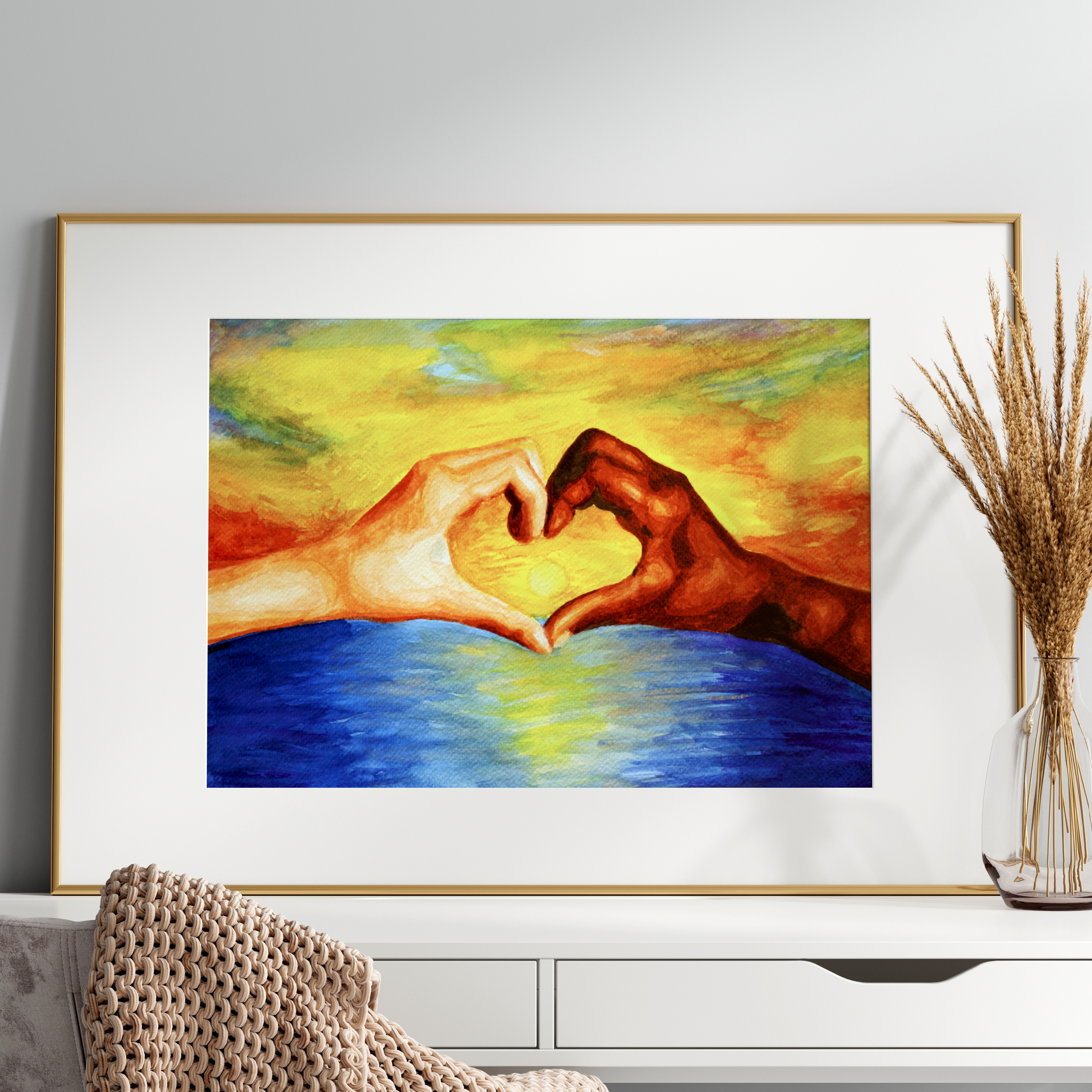 Framed artwork of two hands making a heart shape over water on a white wall.