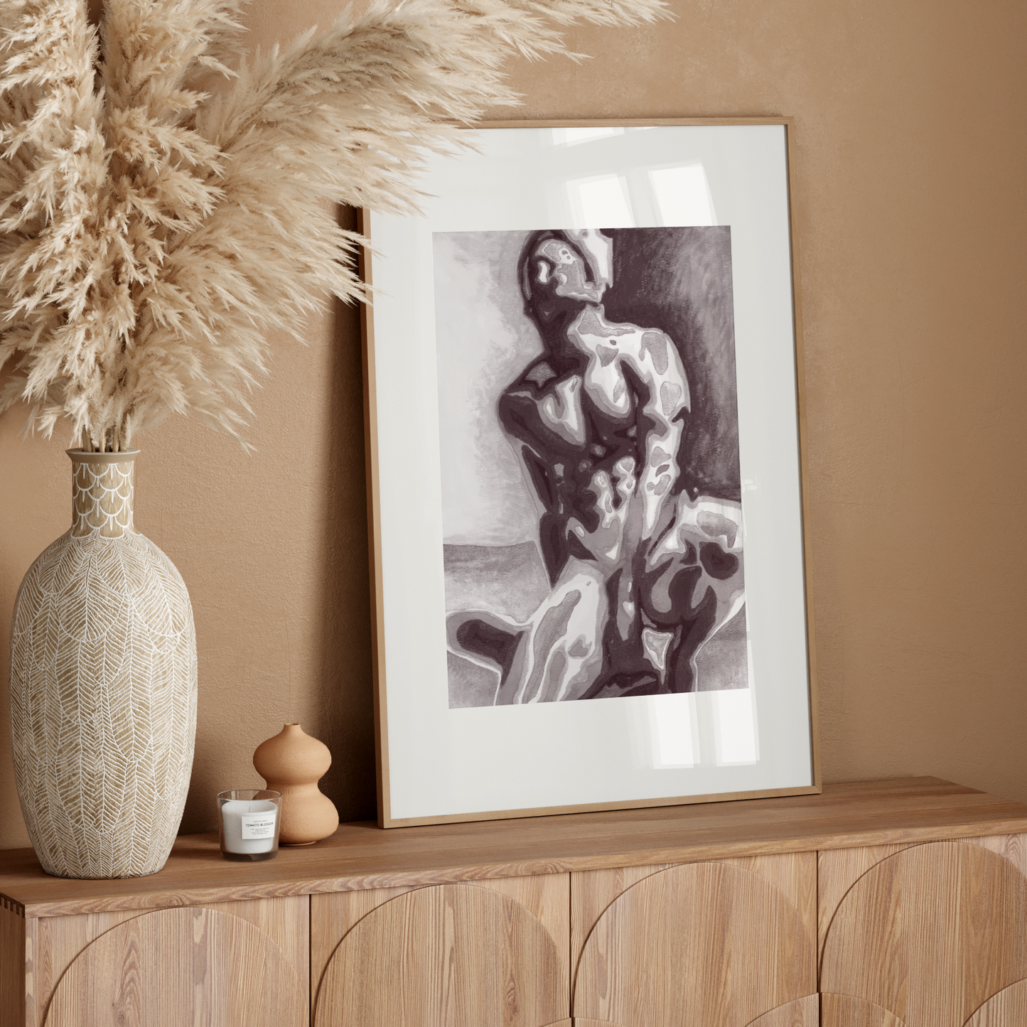 Decorative setup with a vase, candle, and framed artwork on a wooden console against a beige wall.