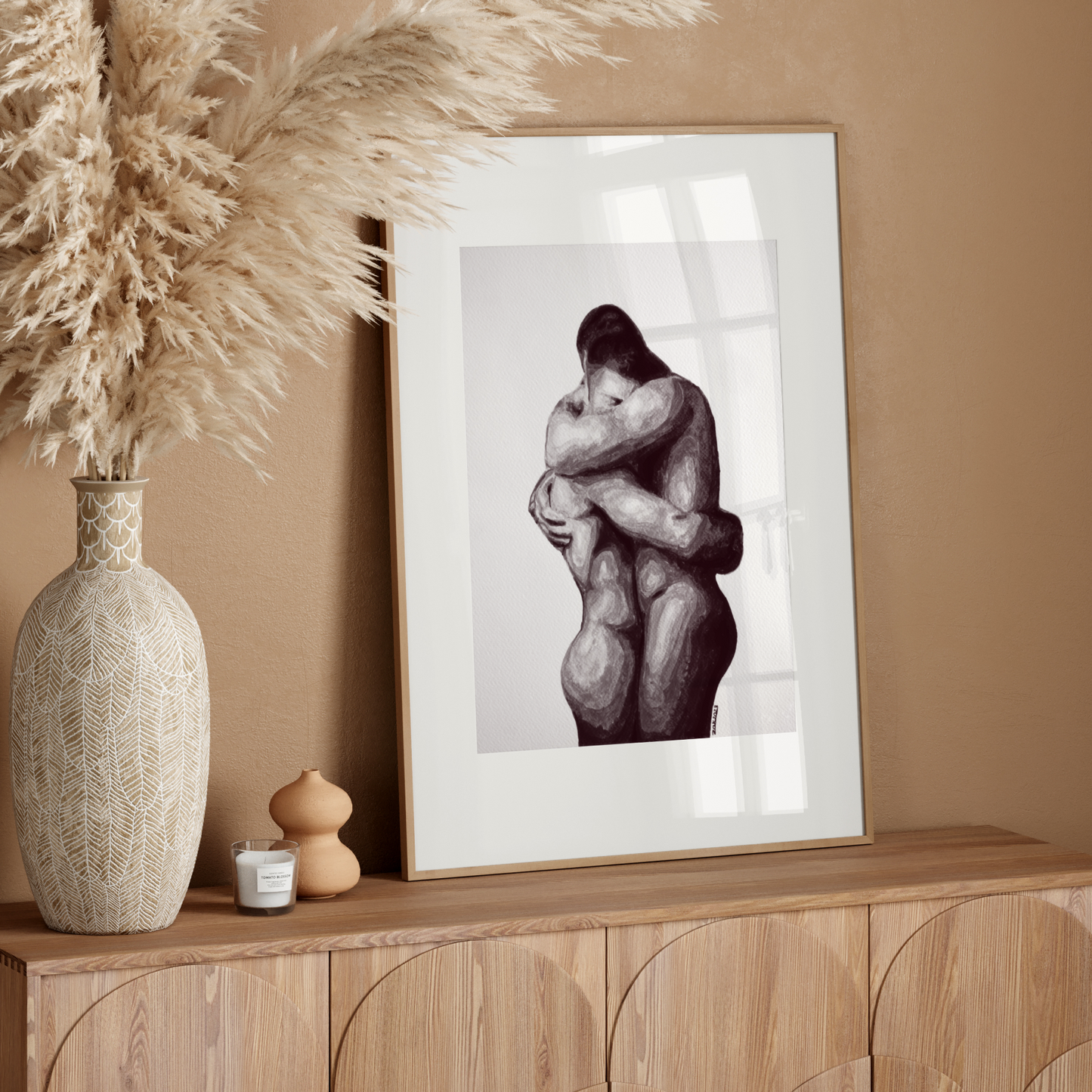 Framed artwork of two embracing figures on a wooden sideboard with decorative elements.