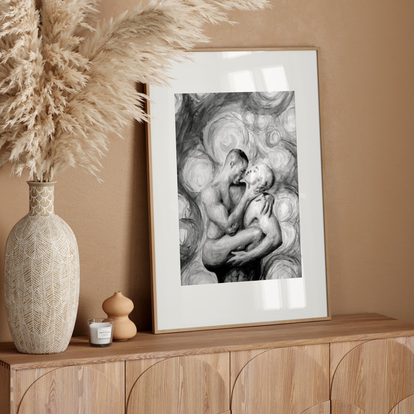 Framed artwork on a wooden sideboard with decorative vase and pampas grass.
