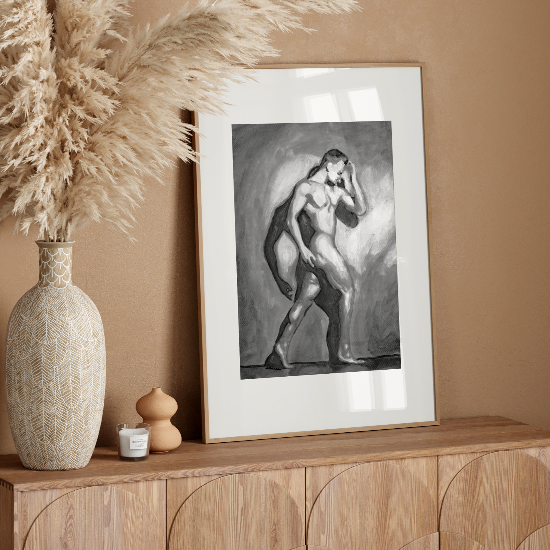 Framed artwork on a wooden console table with decorative vase and pampas grass against a beige wall.