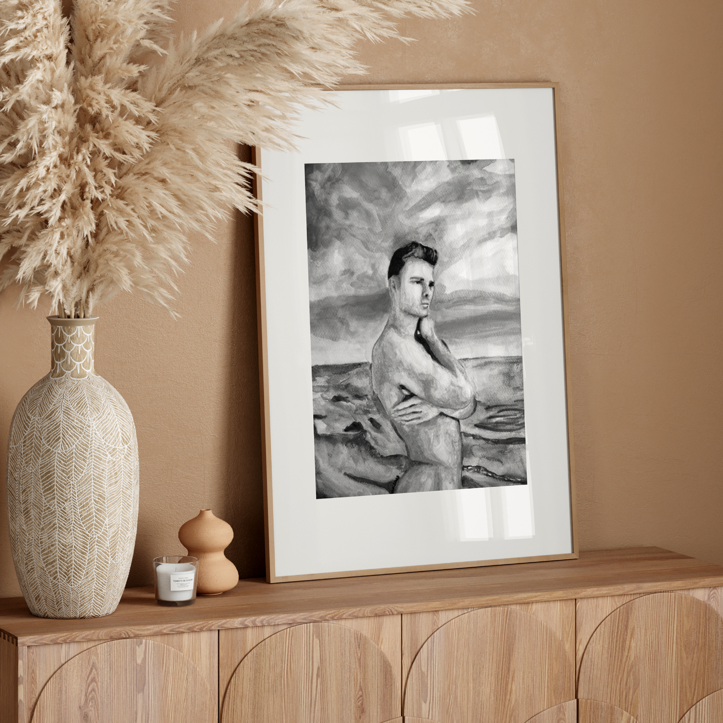 Framed artwork on a wooden console table with decorative vase and pampas grass against a beige wall.