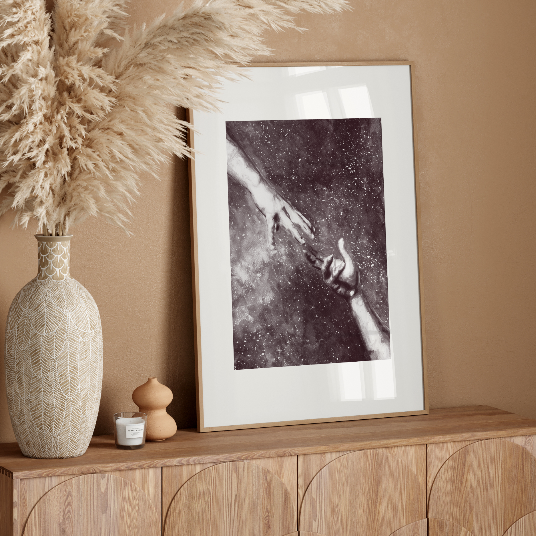 Decorative setup with a vase, dried pampas grass, and framed artwork on a wooden console against a beige wall.