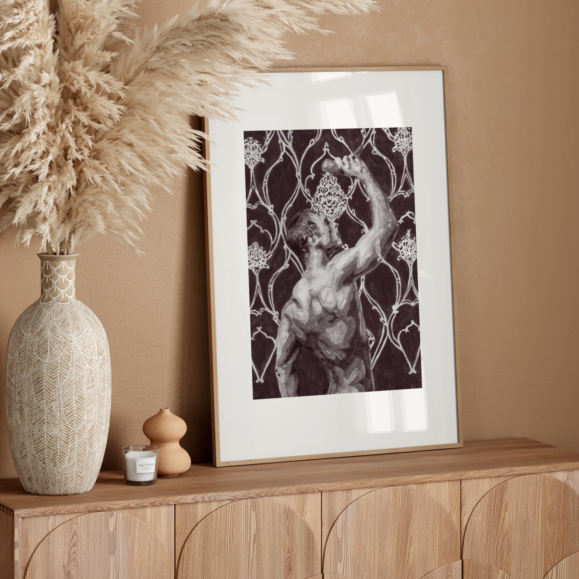 Framed artwork on a wooden console table with decorative vase and pampas grass against a beige wall.