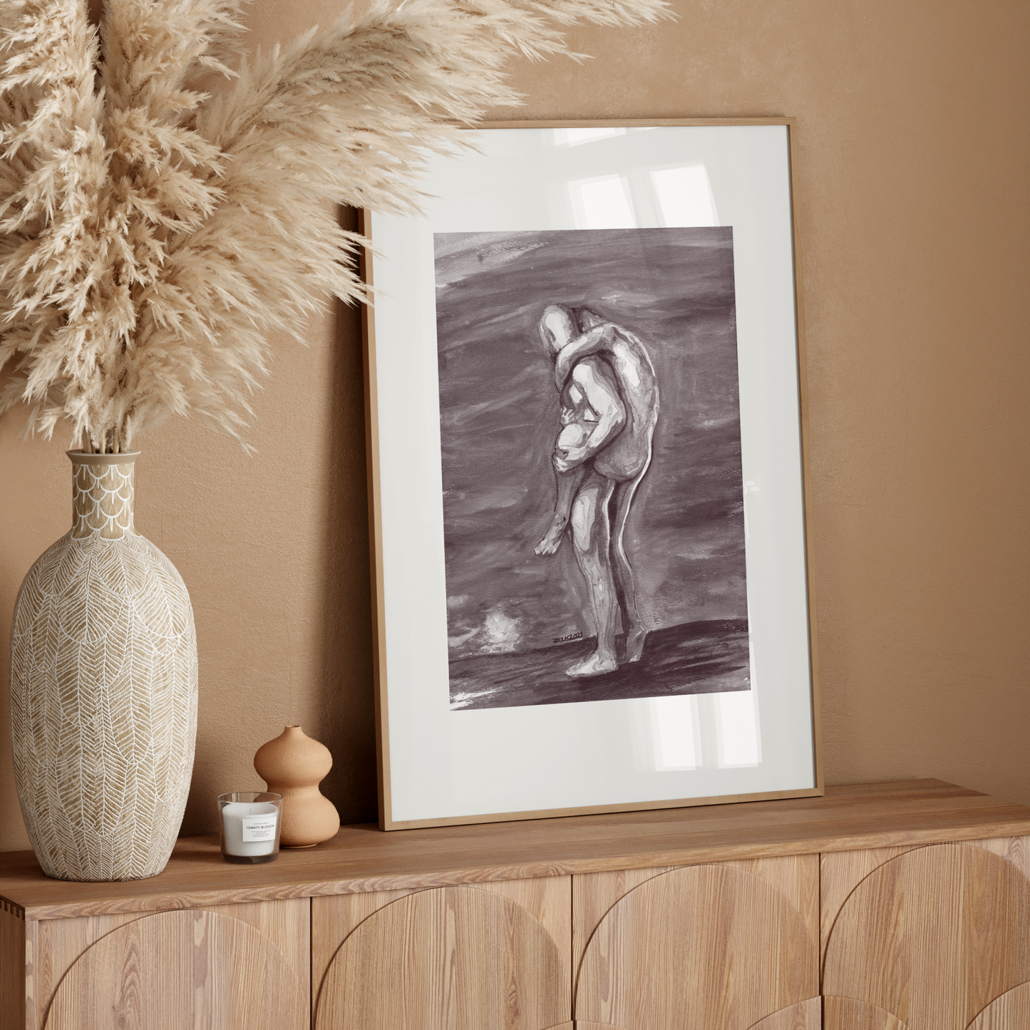 Decorative setup with a vase, candle, and framed artwork on a wooden console against a beige wall.