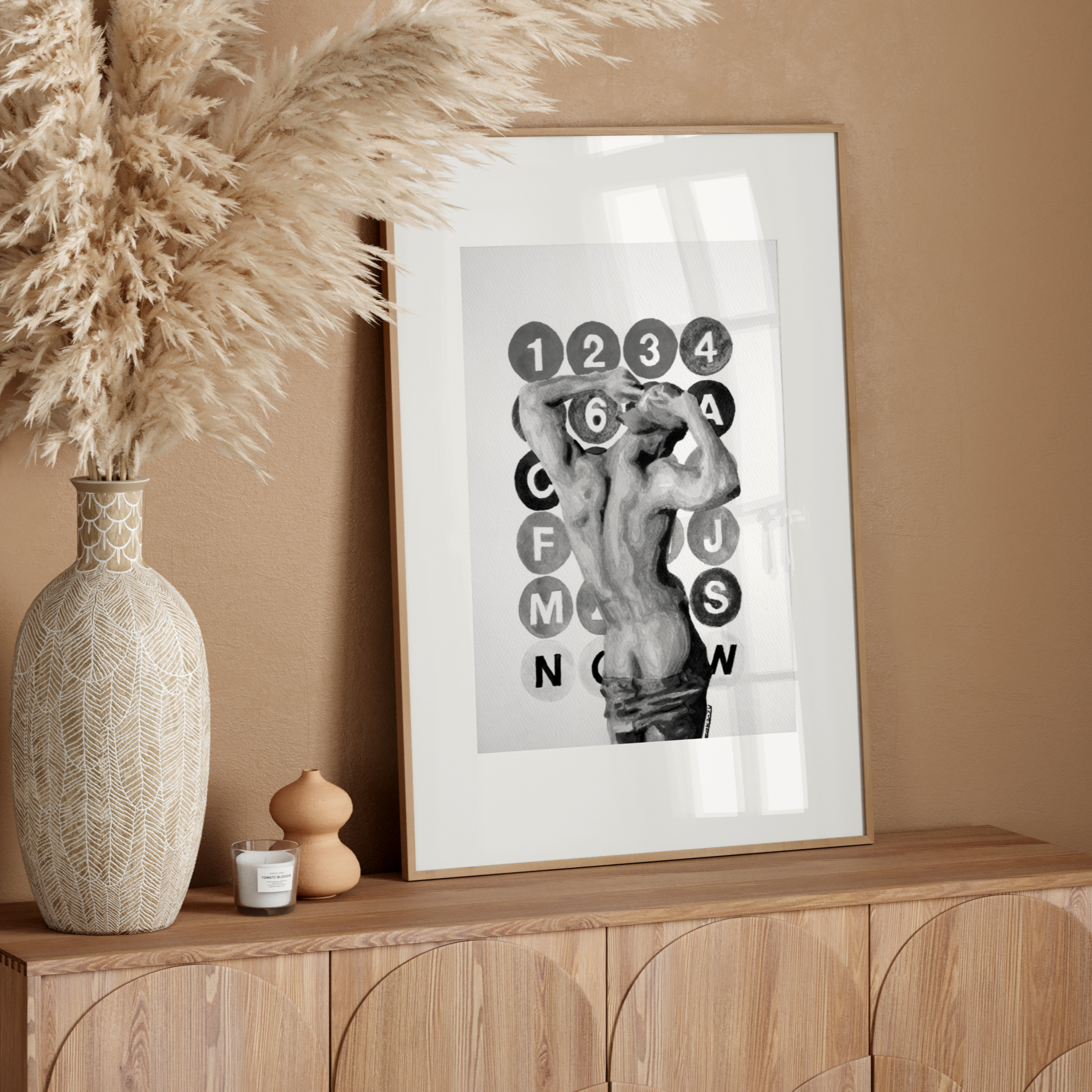 Decorative setup with a vase, candle, and framed artwork on a wooden console against a beige wall.