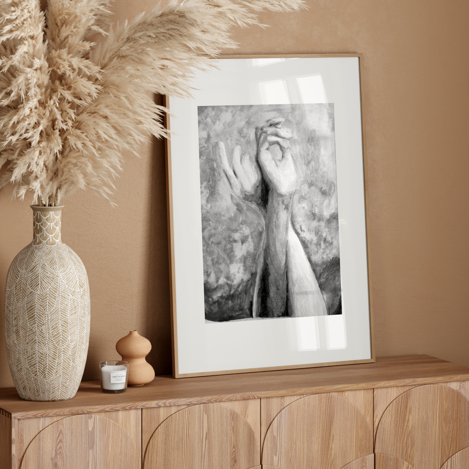 Decorative setup with a vase, dried pampas grass, and framed artwork on a wooden console against a beige wall.