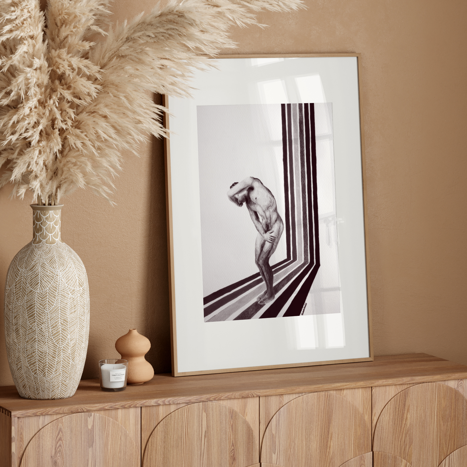 Decorative setup with a vase, candle, and framed artwork on a wooden console against a beige wall.