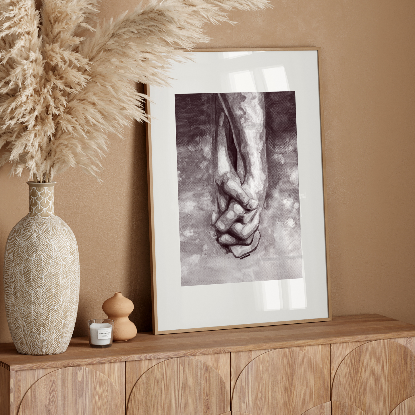 Framed artwork of hands holding each other on a wooden sideboard with decorative elements.