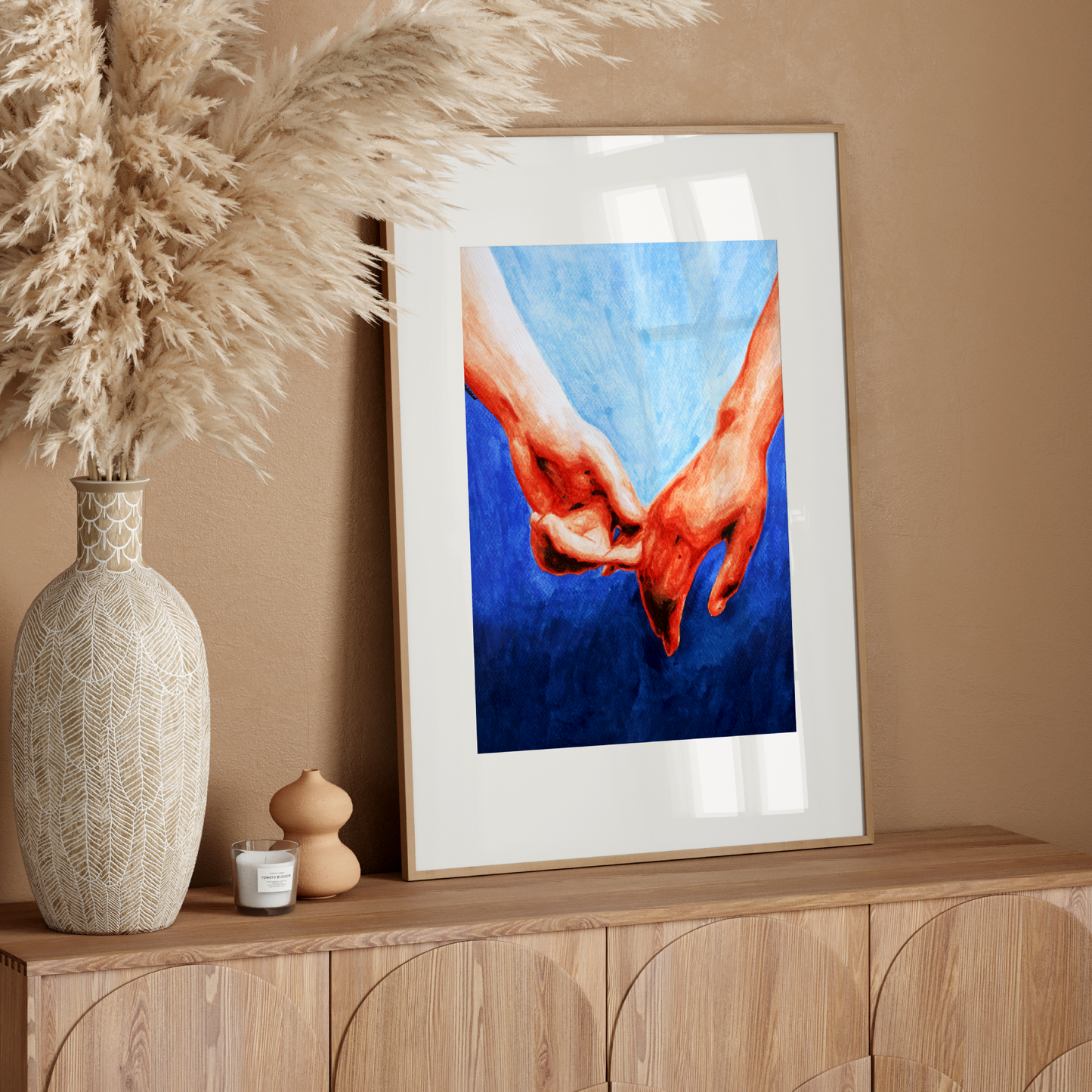 Framed artwork of hands holding each other on a wooden console table with decorative elements.
