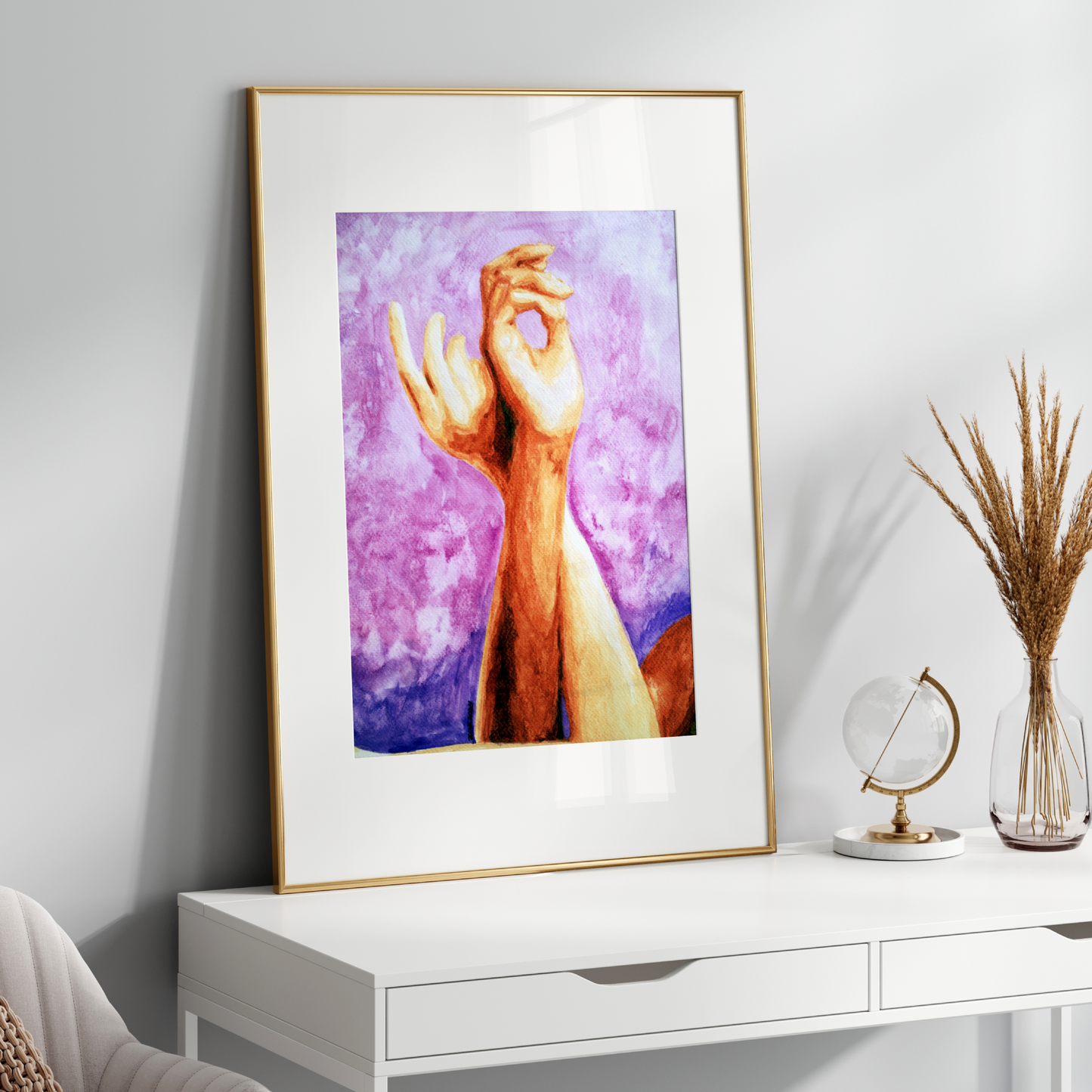 Framed artwork of a hand on a white surface with decorative items.